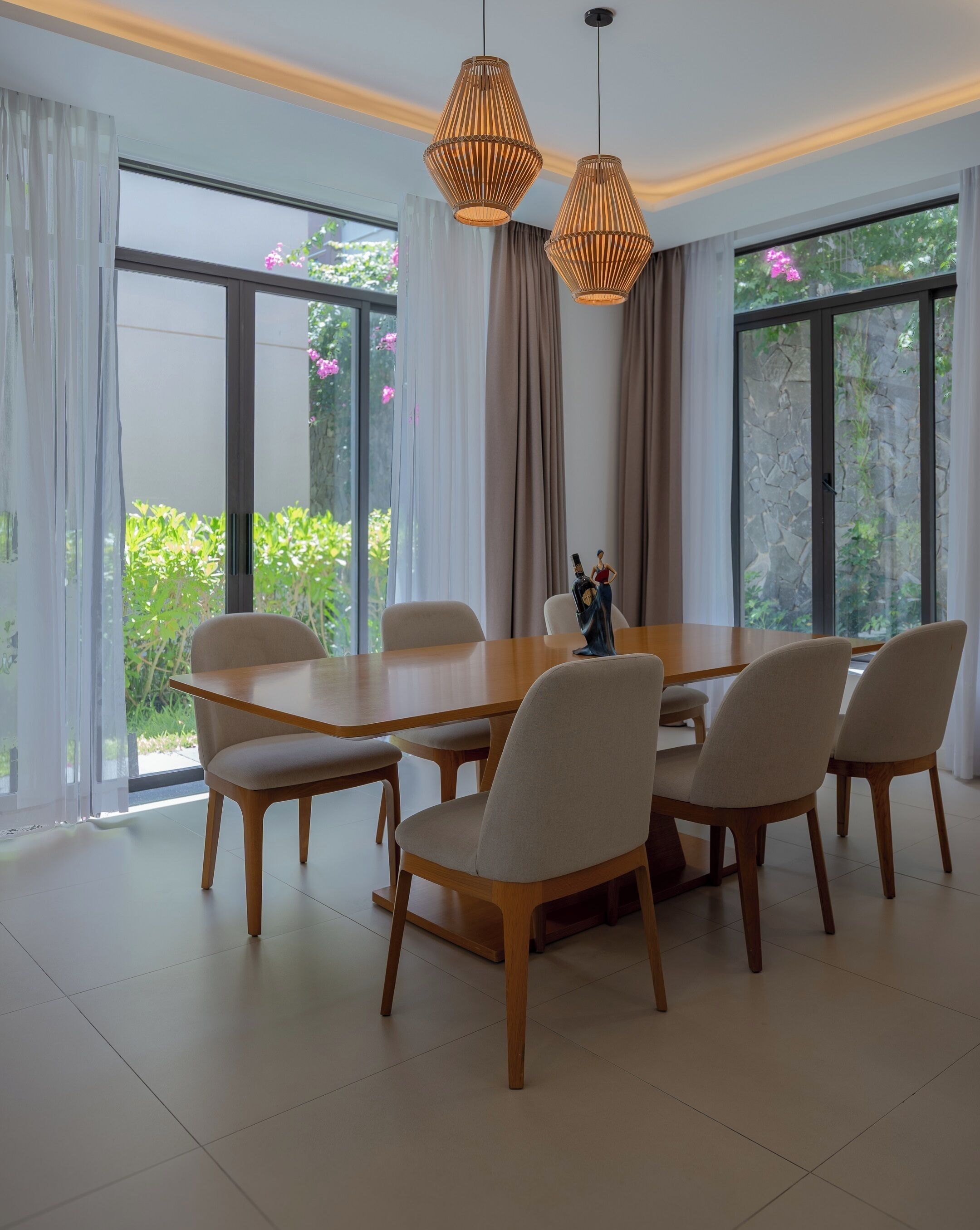 A dining area with a large wooden table, six chairs, and two hanging pendant lights.
