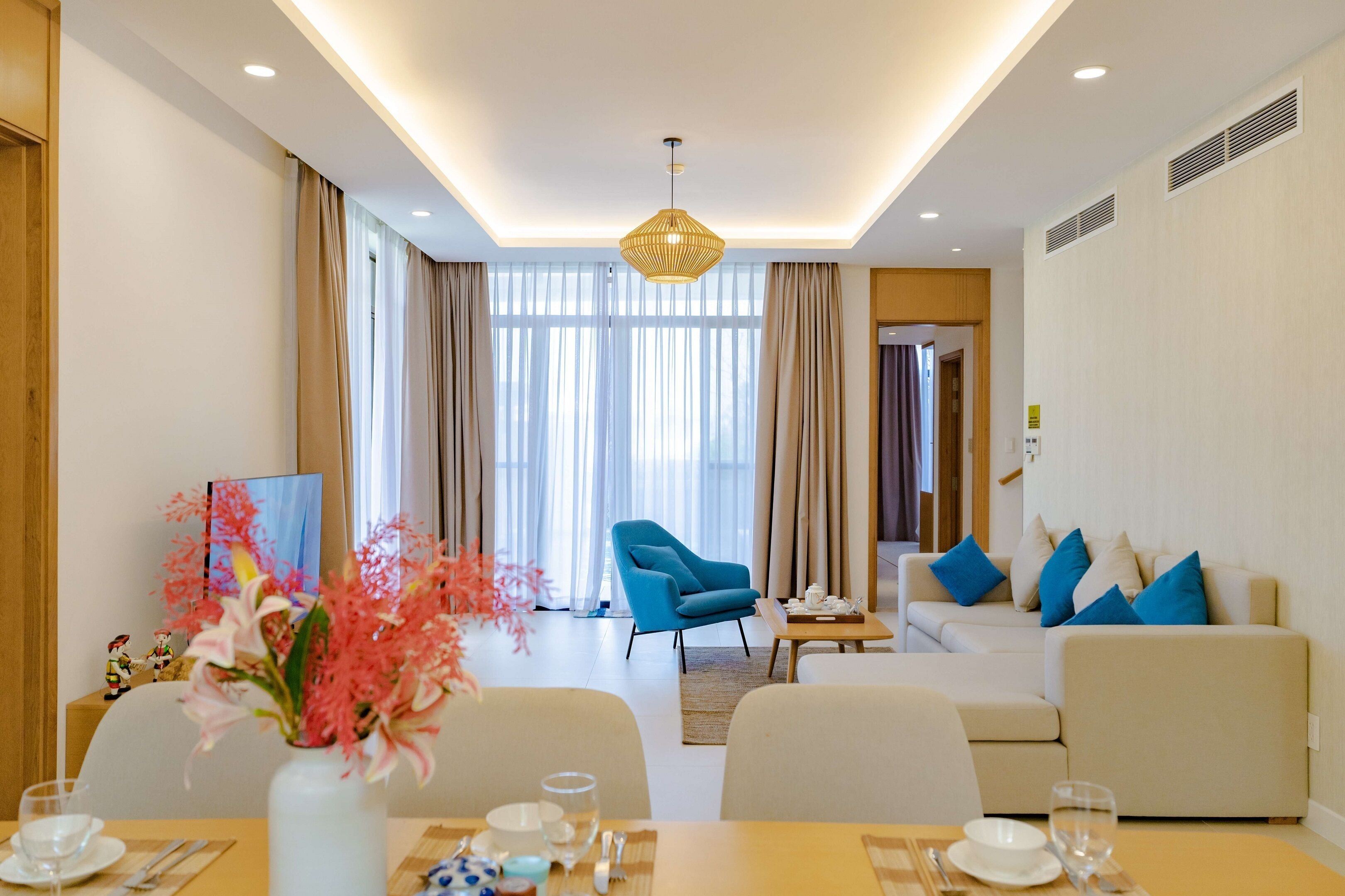 A modern living room with a sofa, armchairs, and a dining area with a table set for two.