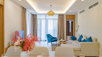 A modern living room with a sofa, armchairs, and a dining area with a table set for two.