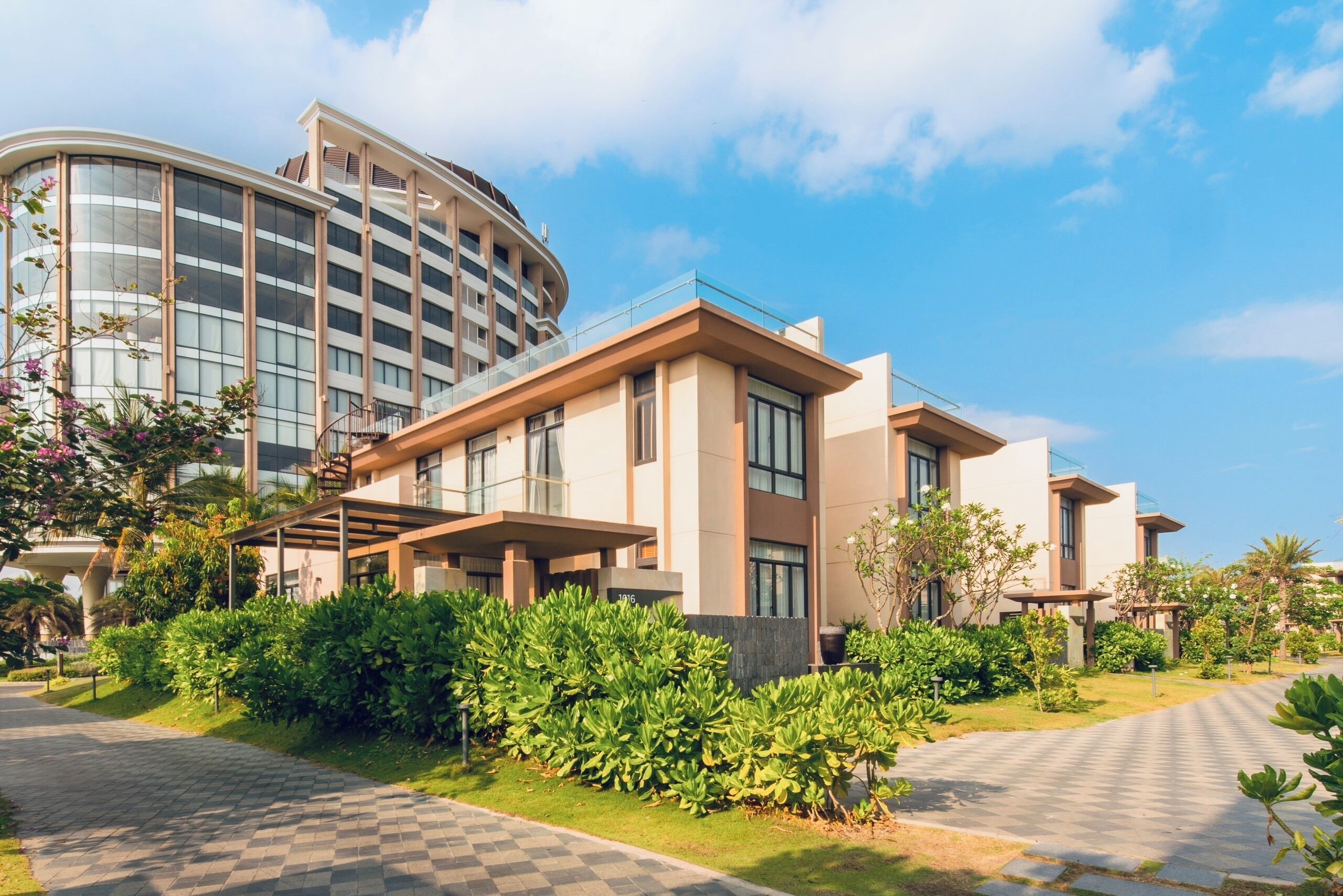 A modern hotel with a curved glass facade, a covered outdoor area, and well-maintained greenery.