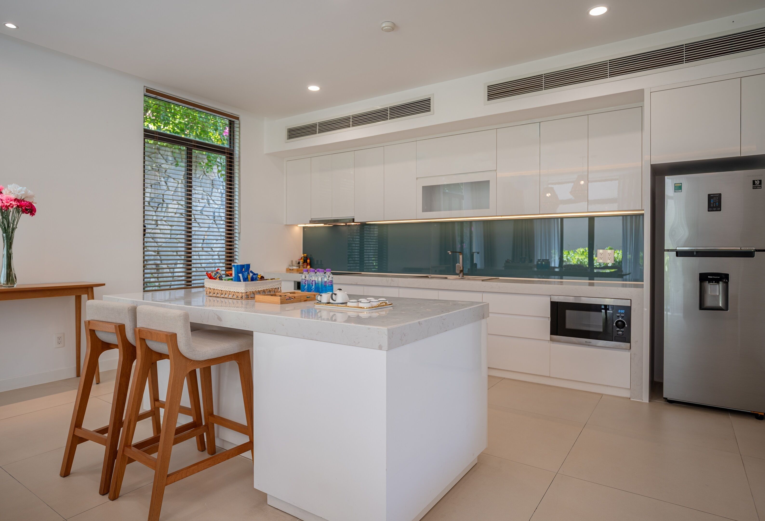 A modern kitchen with white cabinetry, a central island with bar stools, a built-in microwave, and a stainless steel refrigerator.