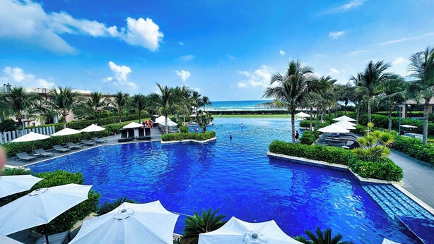 A large swimming pool with a view of the ocean, surrounded by palm trees and lounge chairs. - Hese Pool Villas & Resort Cam Ranh (Cam Lam)