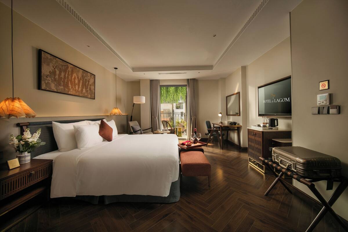 Een hotelkamer met een groot bed, nachtkastjes, een bureau, een televisie en uitzicht op groen.