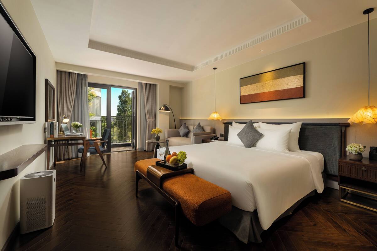 Een moderne hotelkamer met een groot bed, een bureau met computer, een televisie en een balkon met gordijnen.