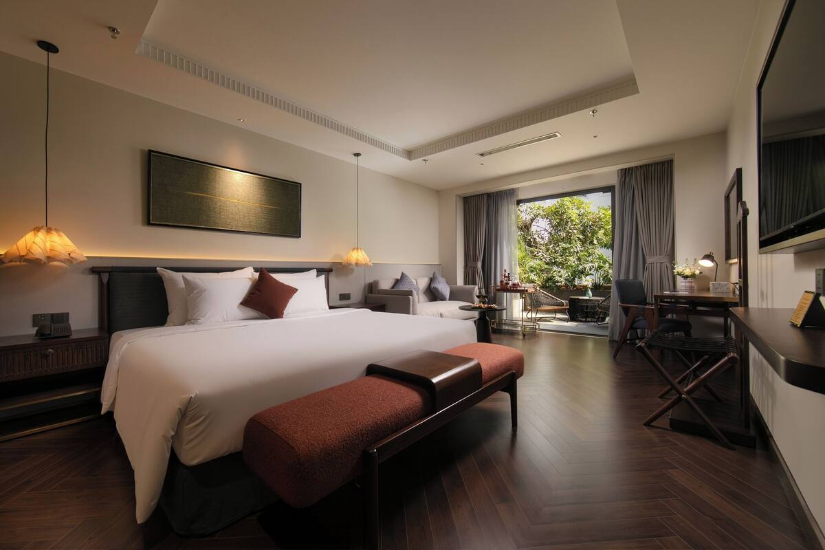 Een moderne hotelkamer met een groot bed, een bureau, een zithoek en een balkon met uitzicht op groen.