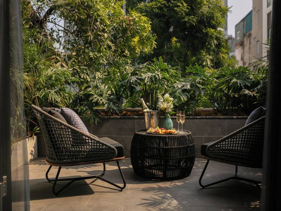 Une terrasse dotée de chaises en osier et d’une table ronde, entourée d’une végétation luxuriante et avec une vue sur la ville en arrière-plan.