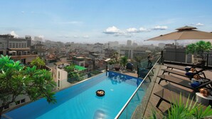 Una piscina sul tetto con vista chiara sulla città, circondata da vegetazione e arredata con lettini e ombrelloni.