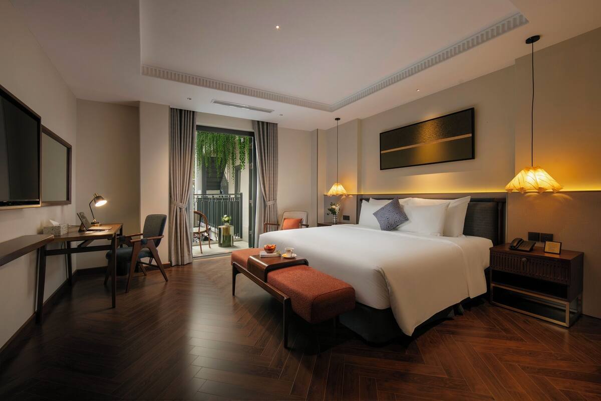 Een moderne hotelkamer met een groot bed, een bureau met lamp, een bankje en uitzicht op het landschap.