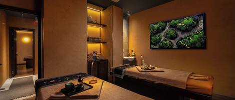 A spa room with two massage tables, a wall-mounted artwork, and a shelf with toiletries.