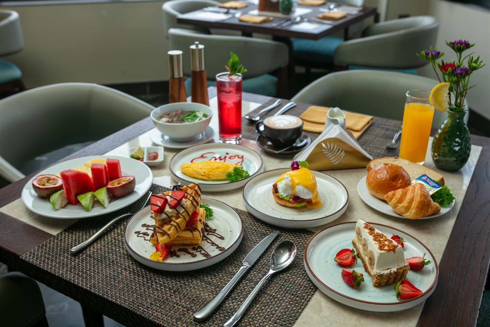 Una colazione con diversi piatti, tra cui waffle, uova, croissant e frutta.