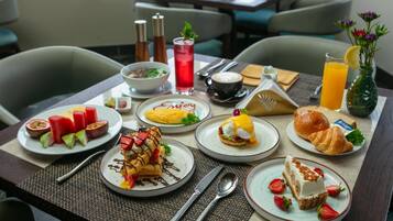 Una colazione con diversi piatti, tra cui waffle, uova, croissant e frutta.