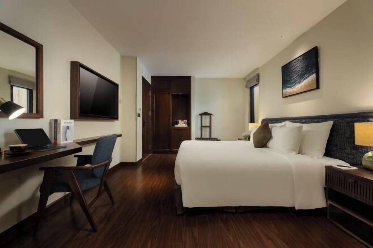 Een hotelkamer met een bed, bureau, stoel, televisie en kunstwerk.