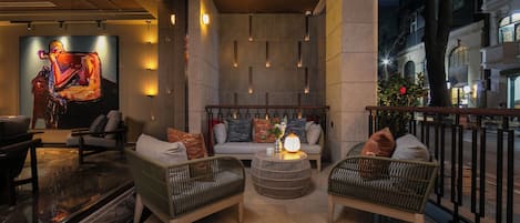 A modern lounge area with wicker furniture, a central round table, and a large abstract painting on the wall.