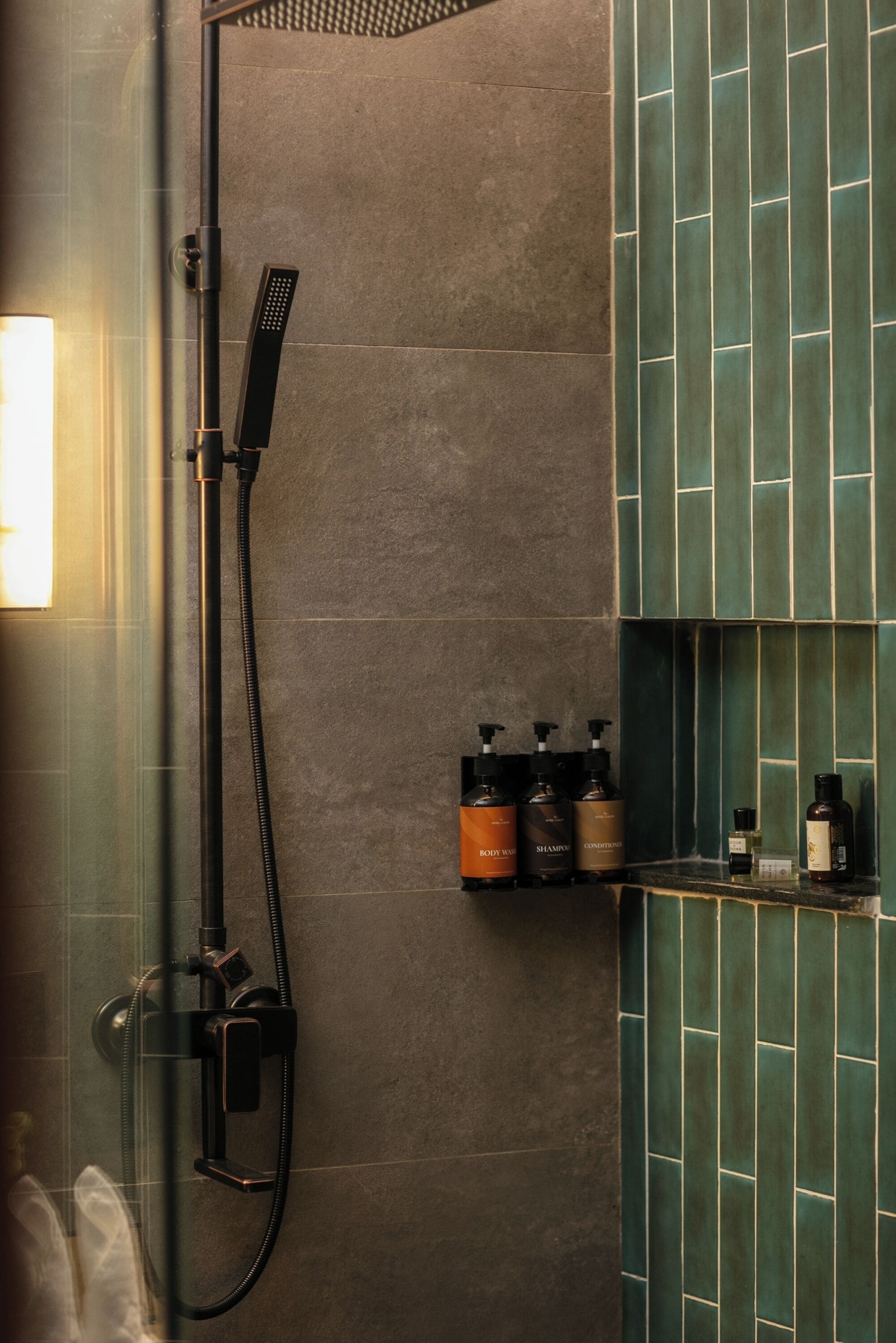 A shower area with a glass enclosure, a handheld showerhead, and a selection of toiletries on a shelf.