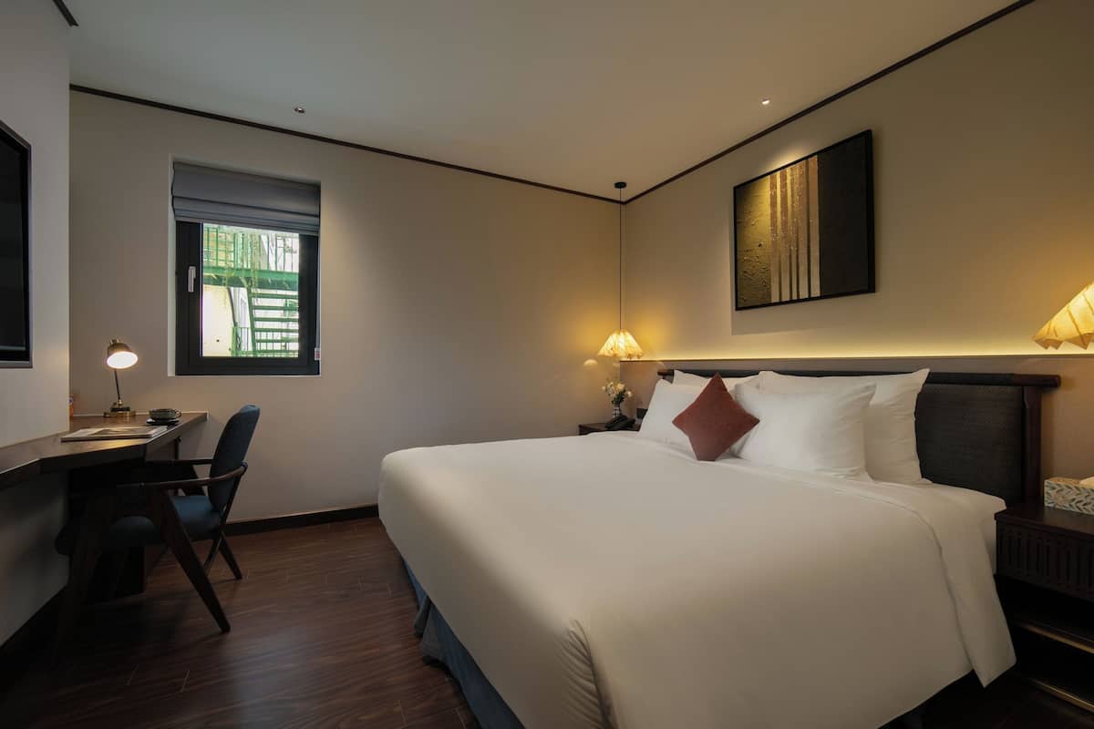 Een hotelkamer met een groot bed, een bureau met stoel, een raam en twee bedlampjes.