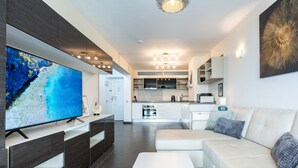 A modern living room with a flat-screen TV, a sofa, and a kitchen in the background. - Stylish Retreat: 1-Bed, Pool, Sleeps 3 REF001 (Benalmádena)