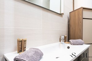 Une salle de bain avec un lavabo blanc, deux bouteilles de shampoing, une serviette et un miroir.
