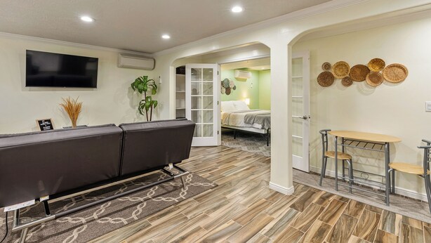 A hotel room with a sofa, a TV, a bed, a small table, and a wall-mounted shelf with decorative plates.