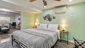 A bedroom with a bed, two bedside lamps, a ceiling fan, an air conditioning unit, and a decorative wall piece.