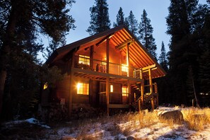 Une cabane en rondins dotée d’un balcon, entourée de grands arbres et de neige.