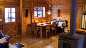 Un acogedor interior de cabaña con comedor, sofá, chimenea y un ventanal grande.
