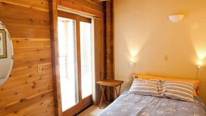 Una habitación de cabaña de madera con una cama, una mesita pequeña y una ventana.