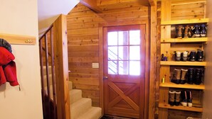 Un interior de madera con puerta de madera, una escalera y estantes con diversos objetos.