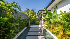 A serene pathway flanked by lush tropical plants leading to a building with a modern architectural style. - Private Pool • Outdoor Showers • Near Beaches (Uluwatu)