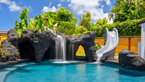Une piscine dotée d’une cascade et d’un toboggan, entourée d’une végétation tropicale.