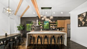 Une cuisine moderne dotée d’un îlot central, de tabourets de bar, de luminaires suspendus et d’une grande fenêtre.