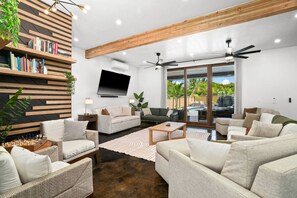 A modern living room with a flat-screen TV, multiple sofas, a coffee table, and a bookshelf. - Private Lagoon Pool and Jacuzzi & Theater! (Princeville)