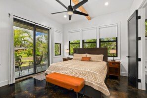 A bedroom with a bed, a bench, a ceiling fan, and a view of a garden. - Private Lagoon Pool and Jacuzzi & Theater! (Princeville)