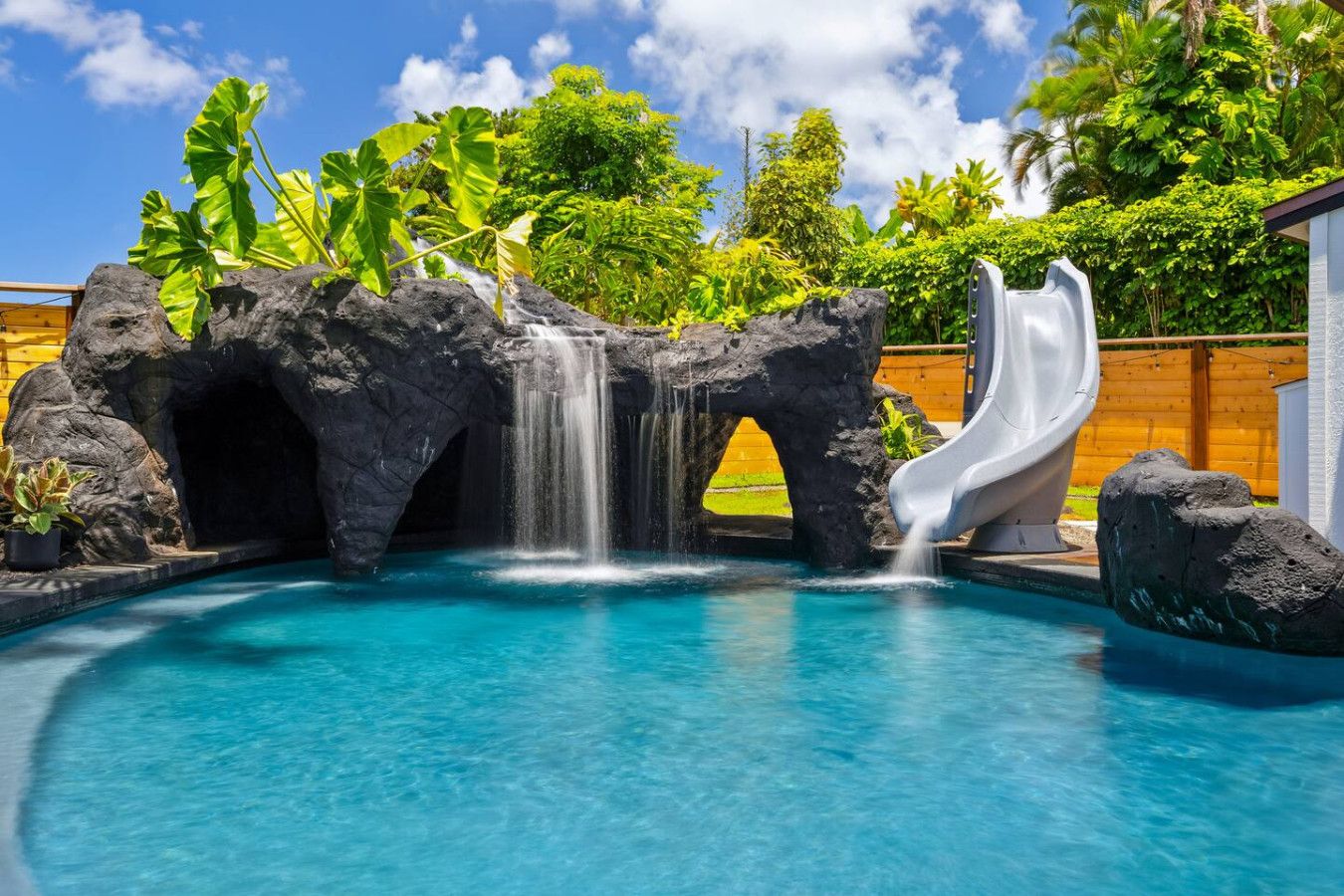 A pool with a waterfall and slide, surrounded by tropical vegetation.
