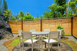 A patio with a round table and chairs, a wooden fence, and tropical vegetation.