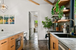 A modern kitchen with wooden cabinets, a marble countertop, a built-in stove, and a hanging plant. - Private Lagoon Pool and Jacuzzi & Theater! (Princeville)