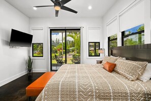 A bedroom with a bed, a TV, a ceiling fan, and a view of a garden through a sliding door.