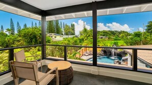 Un balcon abrité offrant une vue sur une piscine, une végétation luxuriante et des maisons situées au loin.