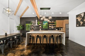 A modern kitchen with a central island, bar stools, pendant lighting, and a large window. - Private Lagoon Pool and Jacuzzi & Theater! (Princeville)