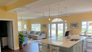 A spacious kitchen with a large island, a dining area with a white table, and a living room with a gray sofa. - Intracoastal Waterfront Retreat, Sleeps 10 (Holly Hill)