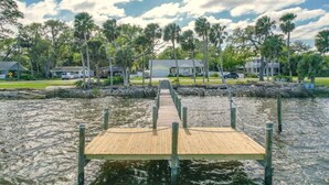 A wooden dock leading to a house surrounded by palm trees and a calm body of water. - Intracoastal Waterfront Retreat, Sleeps 10 (Holly Hill)