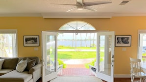 A room with a sliding glass door leading to a patio, a ceiling fan, and a view of a grassy area and water. - Intracoastal Waterfront Retreat, Sleeps 10 (Holly Hill)