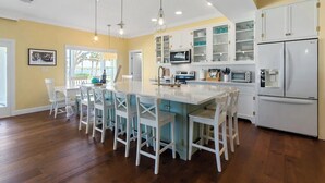A modern kitchen with white cabinetry, a central island with bar stools, and a built-in microwave. - Intracoastal Waterfront Retreat, Sleeps 10 (Holly Hill)