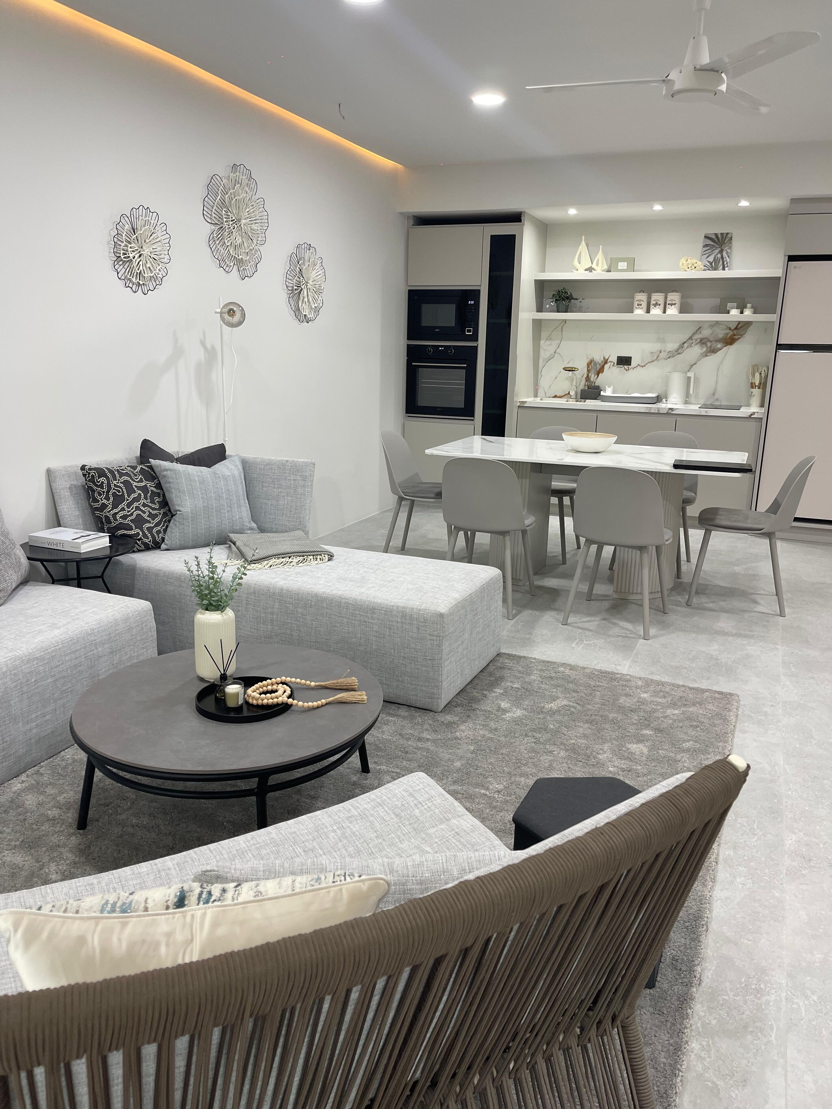 A modern living room with a grey sofa, a round coffee table, and a dining area with a white table and chairs.