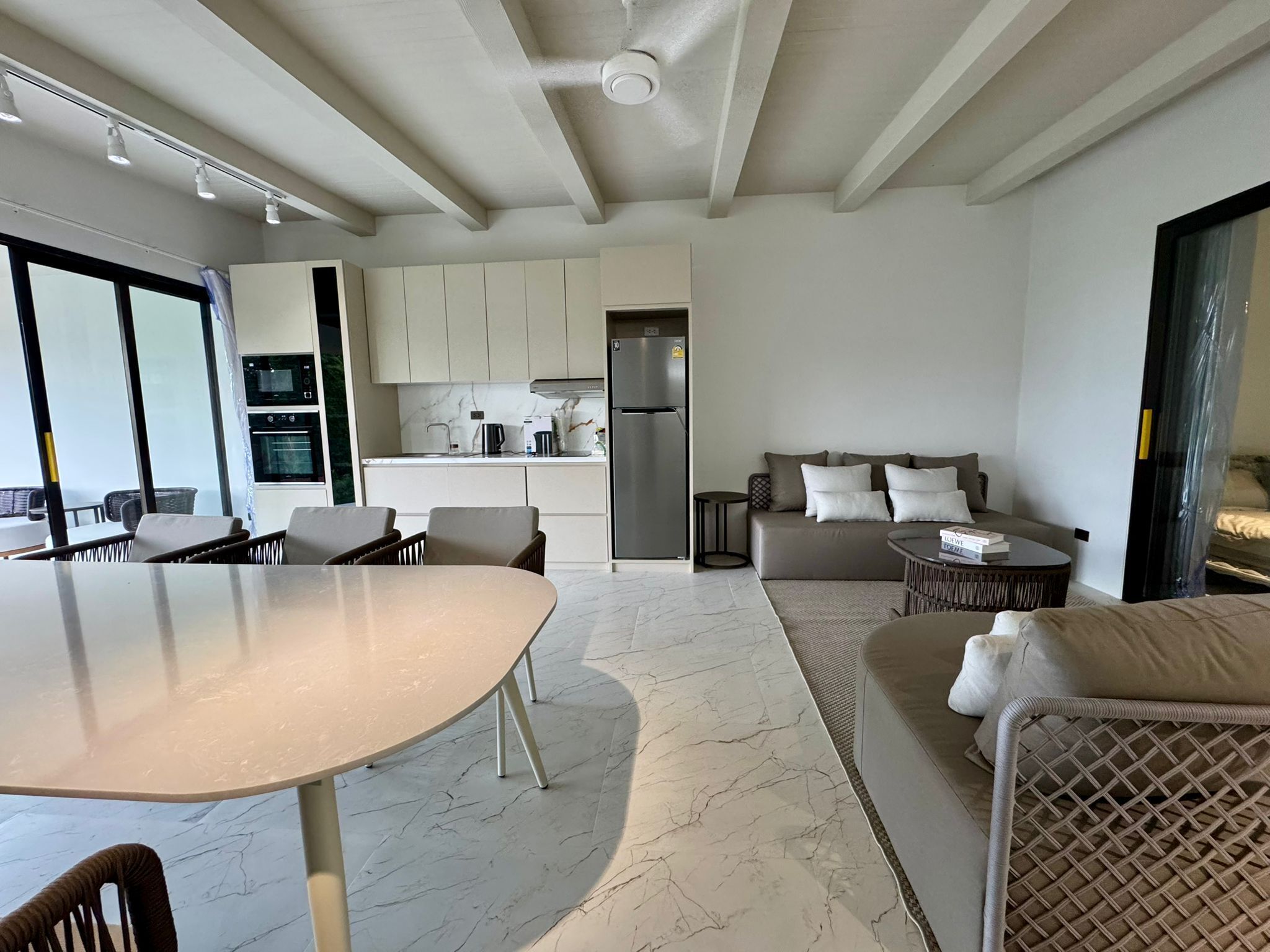 A modern living room with a marble floor, a dining area with a round table, and a kitchen with white cabinets and stainless steel appliances.