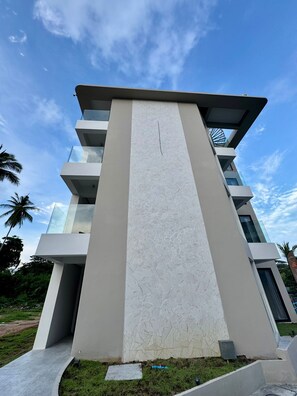 A modern multi-story building with a central vertical feature, balconies, and a clear sky.