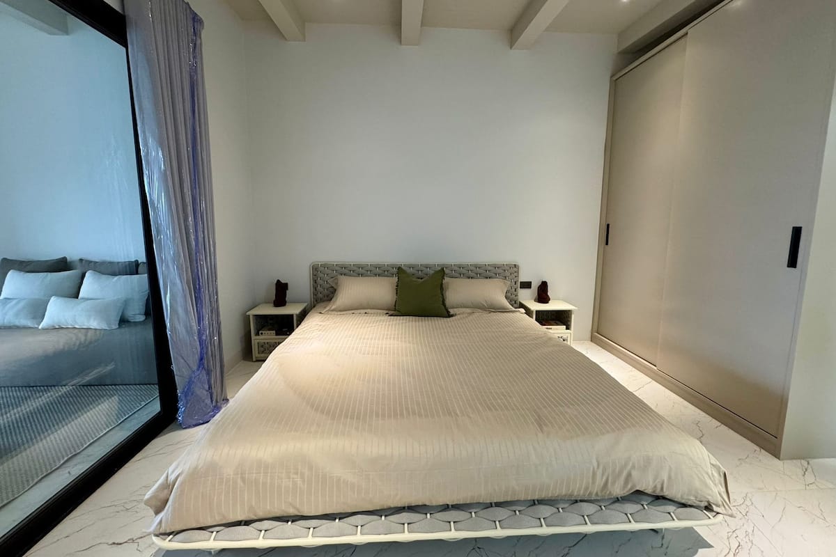 Un dormitorio moderno con una cama grande, dos mesitas de noche y un cabecero, además de una puerta corredera.