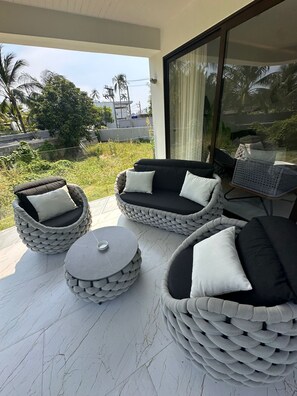 A modern outdoor seating area with wicker furniture and a glass door leading to a lush garden.