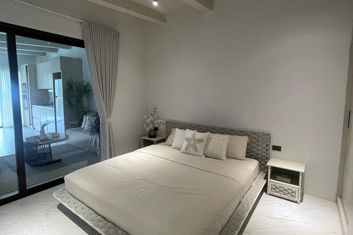 Un dormitorio con una cama grande, un ventilador de techo, una mesita de noche y vistas al área de estar a través de una puerta de cristal.