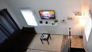 A living room with a sofa, a coffee table, a TV mounted on the wall, and a staircase leading to an upper floor. - Cozy Cabin • 5 mins from Cave Tubing & Zipline (Frank's Eddy)