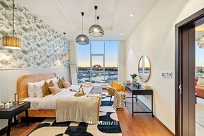 A modern bedroom with a large bed, a view of the city, and a desk with a chair. - 3B-TiaraRuby-106 (Dubai)